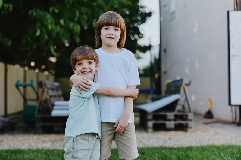 Two cheerful boys embracing in a sunny backyard, showcasing a strong bond of friendship and joy during a warm day outdoors, creating a playful atmosphere.