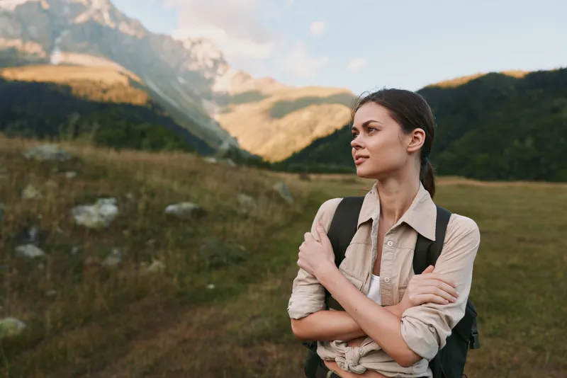 A woman hiker stands in a sunlit valley with a backpack, gazing into the distance. An outdoor scene highlighting resilience, exploration, and connection with nature.