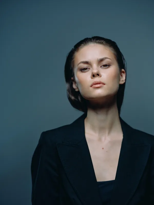 Portrait of a serious woman in black jacket with slicked-back hair against dark background