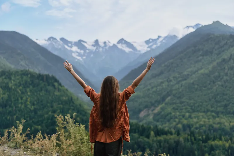 woman mountains nature hiking backview freedom outdoors landscape with arms raised in celebration authenticity inclusivity traveler