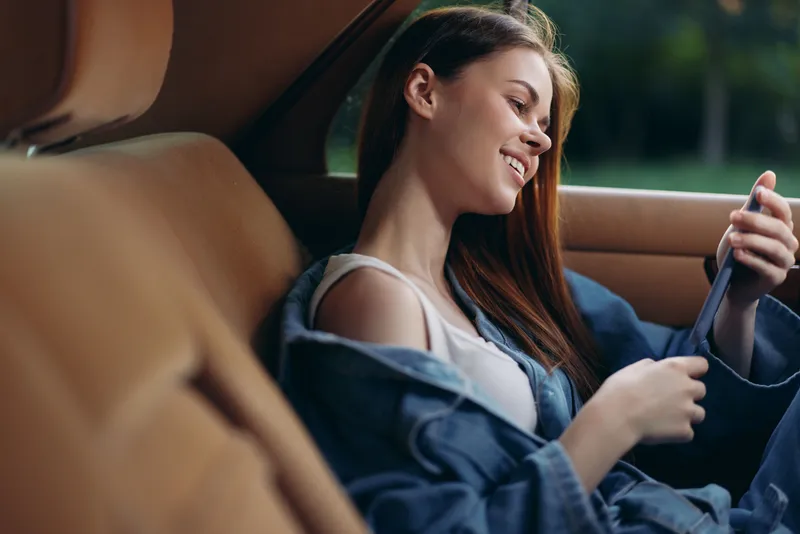Young woman smiling in a denim jacket, sitting in a car, enjoying the view, conveying a sense of freedom and joy, perfect for lifestyle and travel concepts.