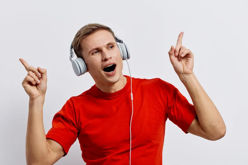 Excited young caucasian man wearing headphones in red t-shirt smile enjoy music listen to audio isolated on white background digital detox concept