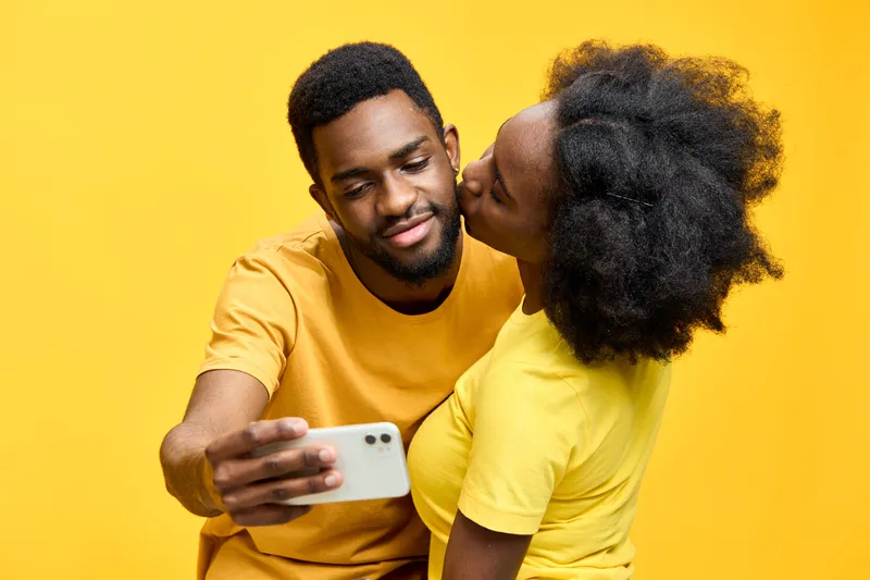 Happy couple taking a selfie together in matching yellow outfits against a bright yellow background, celebrating love and joy