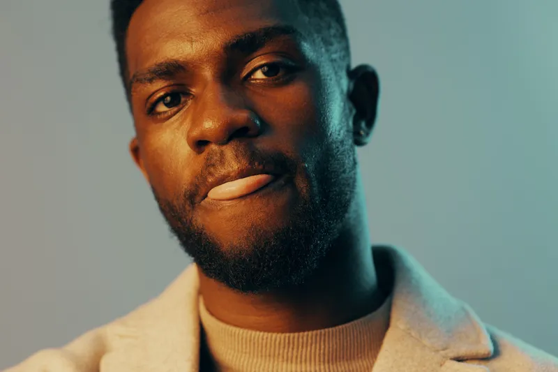 Portrait of a young Black man with a confident expression, wearing stylish casual clothing in warm tones, ideal for lifestyle and fashion concepts