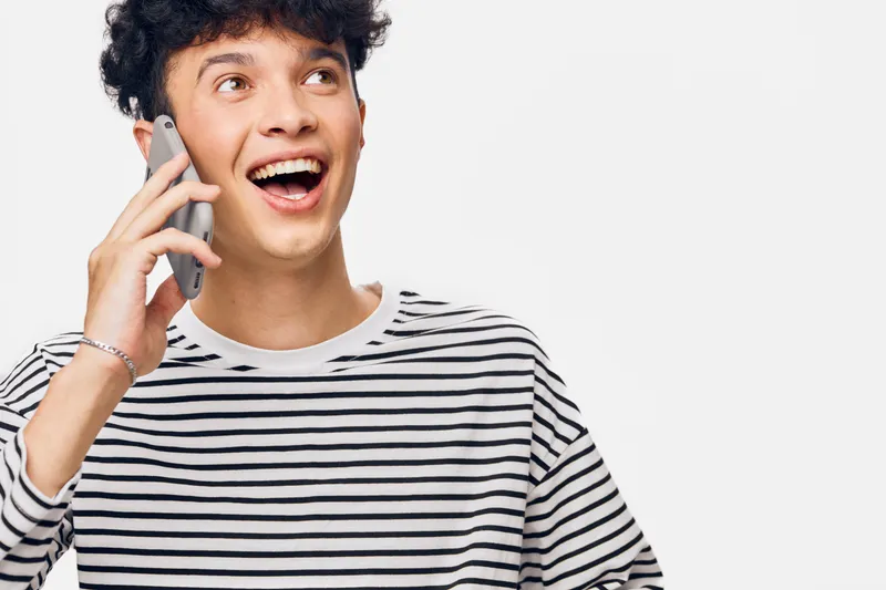 young man talking on phone with excited expression wearing striped shirt on white background showing happiness and communication