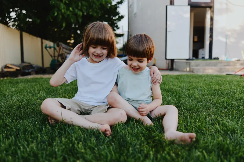 Happy children sitting on green grass, enjoying a sunny day together, sharing smiles and laughter in a playful outdoor setting.