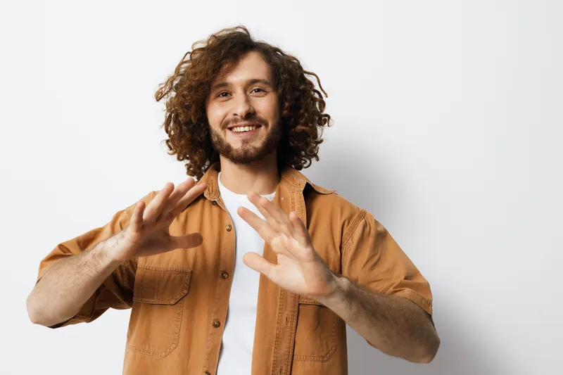 Happy young man with curly hair wearing a casual outfit against a minimalist background, expressing joy and confidence in a modern setting