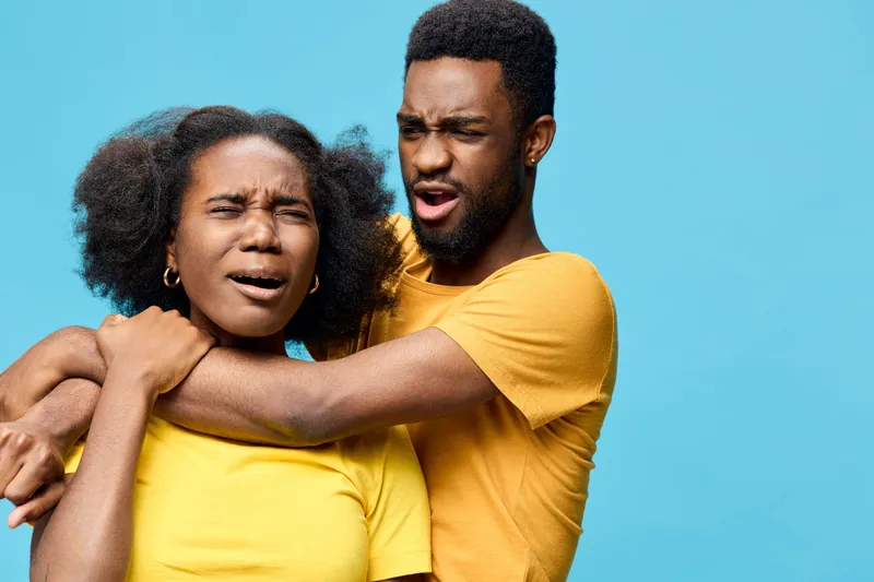 Two young African models express strong emotions in matching yellow shirts against a bright blue background, portraying a dramatic scene of tension and surprise