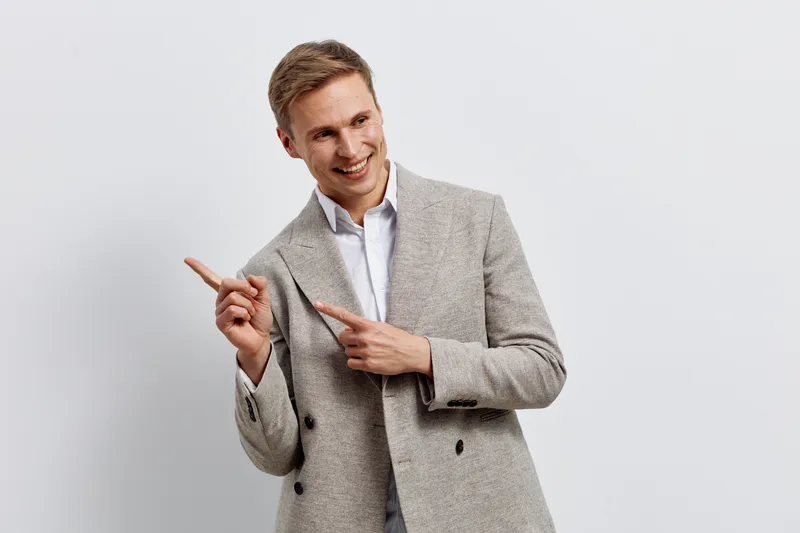 Friendly smiling man in smart casual blazer pointing to the side, appearing confident and approachable isolated on plain white background studio portrait. Business lifestyle concept