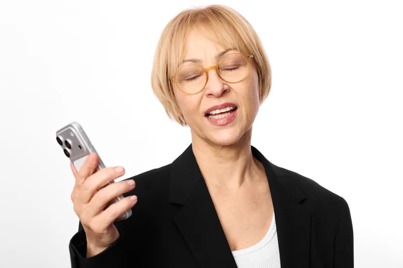 Woman with glasses holding a smartphone, eyes focused down, isolated on clean white background. Business portrait showing communication and technology now.