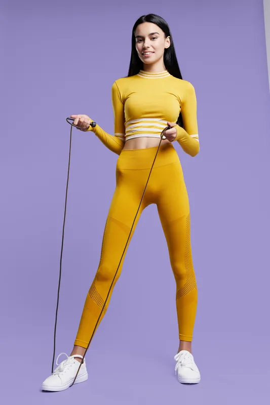 Active woman sport fitness jumping rope in yellow workout clothes, smiling, healthy lifestyle, purple background, youthful and energetic energy.