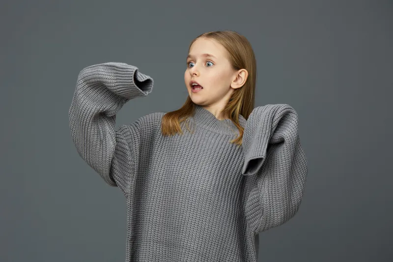 Surprised girl in oversized gray sweater on gray background, showcasing emotions and fashion, ideal for concepts of comfort and spontaneous reactions
