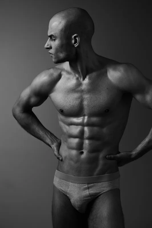Athletic man posing confidently, showcasing a muscular physique in a striking black and white portrait. This image exudes strength and determination in a minimalist style.