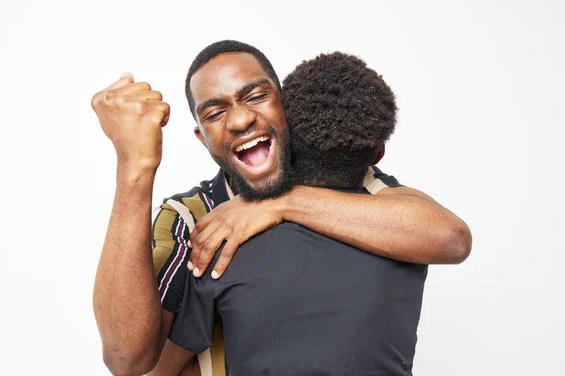 Joyful African American man celebrating while hugging his friend. The vibrant atmosphere highlights connection and happiness, capturing a moment of friendship and support.