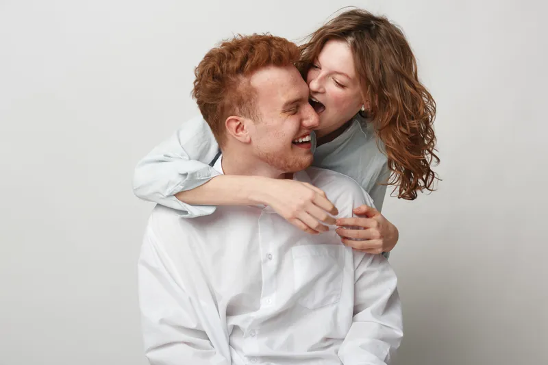 Happy young couple with red hair and curly hair laughing together on white background. Concept of love, friendship, joy, and affectionate relationship between two people.