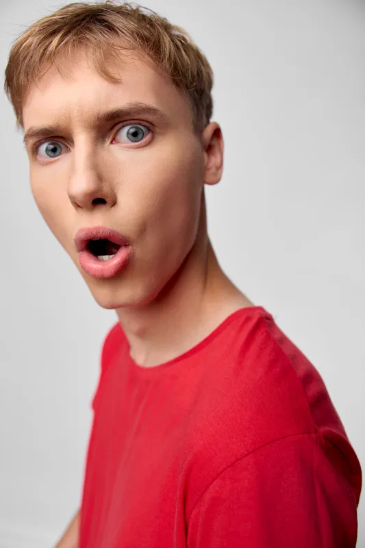 Surprised man in a red shirt with wide eyes and open mouth, closeup expression conveying shock and astonishment in a candid studio photo
