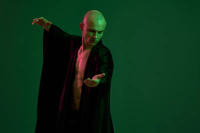 A man gracefully posing in a flowing black robe against a vibrant background, showcasing strength and elegance. This image captures a unique artistic expression of movement and flexibility.