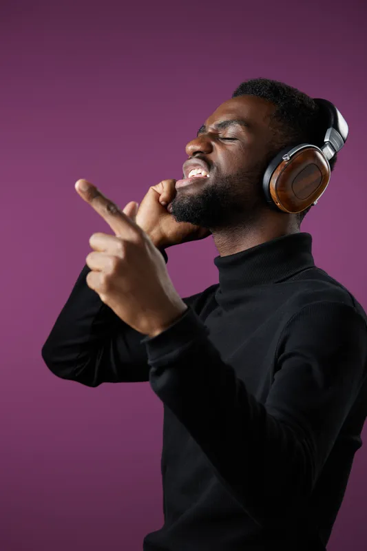 Young Black man enjoying music with headphones on a purple background, expressing joy and rhythm with hand gestures, perfect for lifestyle and music themes