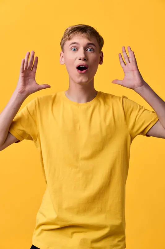 Surprised astonishment excited yellow shirt studio lighting arms raised expression youth casual pose energy and wonder captured in a bright, vibrant, upbeat moment with a male model in a candid