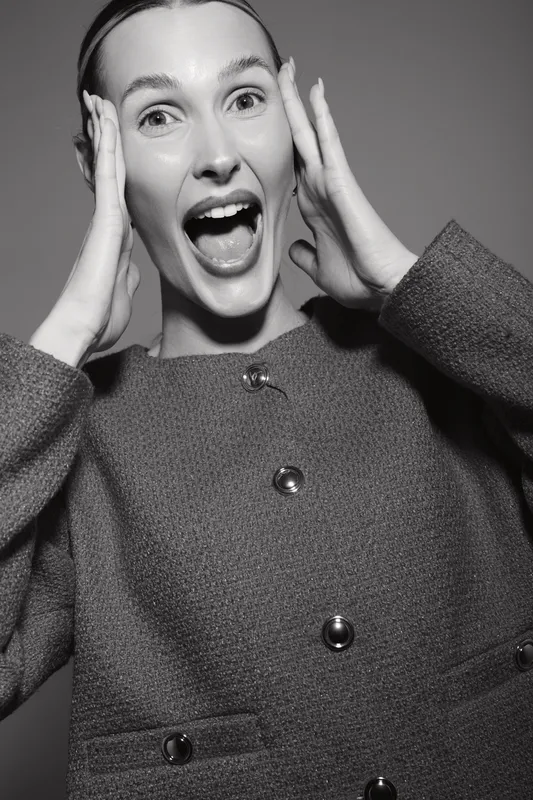 Young Caucasian woman with light skin and pulled back hair looking surprised with hands on face. Studio portrait in black and white with emotional expression.