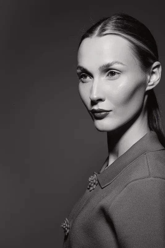 Portrait of a fair skinned young Caucasian woman with slicked back hair wearing a textured sweater, looking sideways with soft high contrast black and white studio lighting.