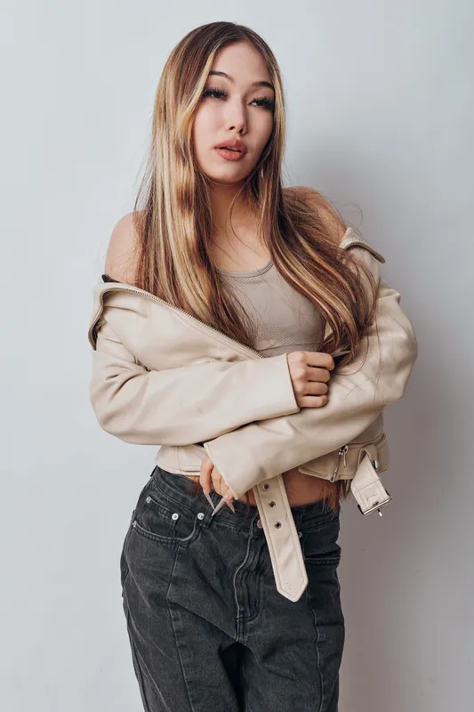Young woman with long hair posing in casual clothes with a jacket over shoulders against neutral background. Fashionable female model standing with confident expression and natural makeup.