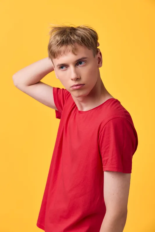 Thoughtful boy in a red shirt stands against a bright yellow background, conveying casual studio fashion and a reflective mood for youth apparel and lifestyle campaigns