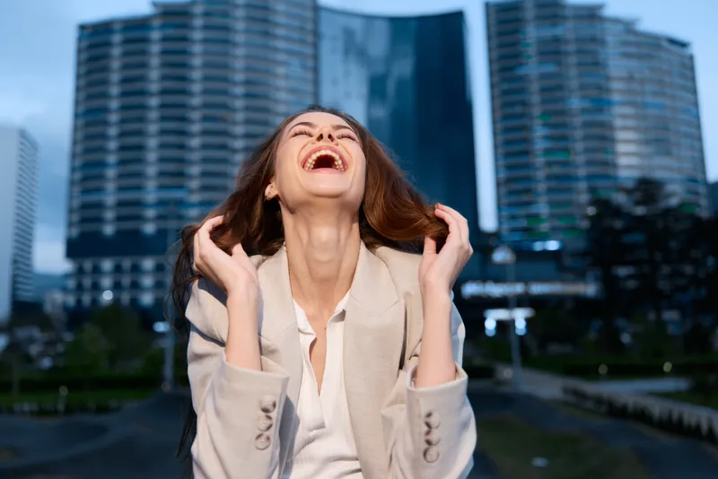Woman laughing joyfully outdoors in business attire with city skyscrapers background, happiness, confidence, urban lifestyle, professional woman
