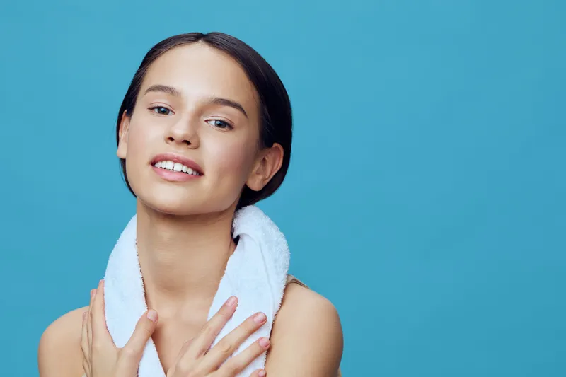 Young woman with a towel smiling against a blue background, exuding confidence and freshness, highlighting beauty and self care concepts
