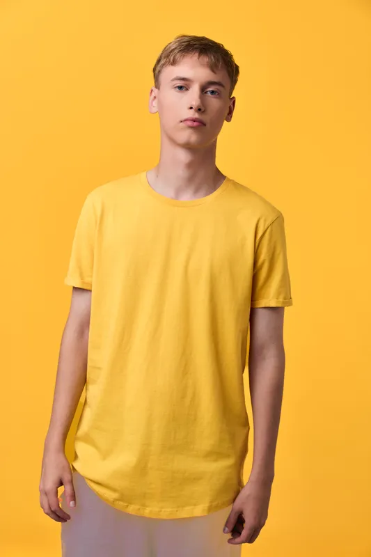 Yellow t shirt wearer standing against bright backdrop, casual fashion shot highlighting color harmony, relaxed posture, and minimal studio styling.