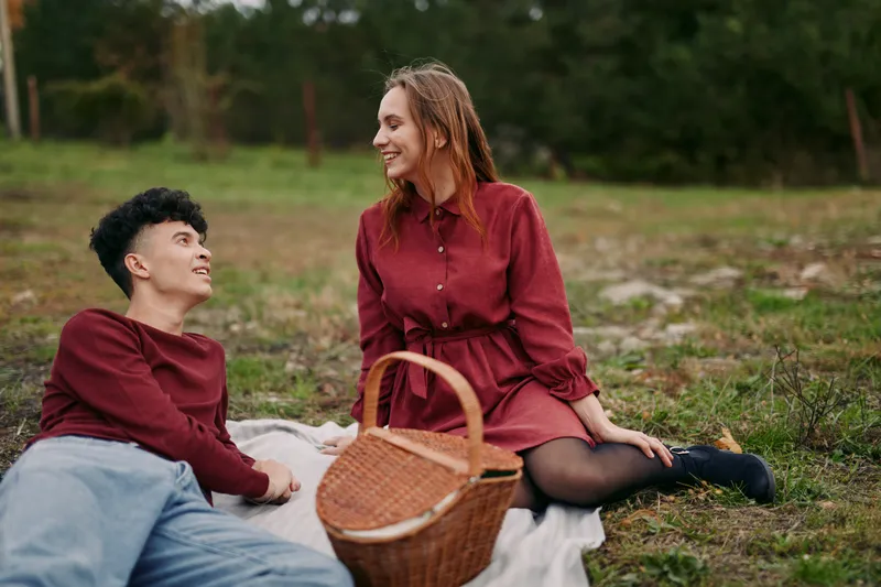Young couple enjoying a candid picnic in a grassy field, sharing genuine smiles and natural interaction that convey authenticity and reliability in a warm, spontaneous outdoor moment.