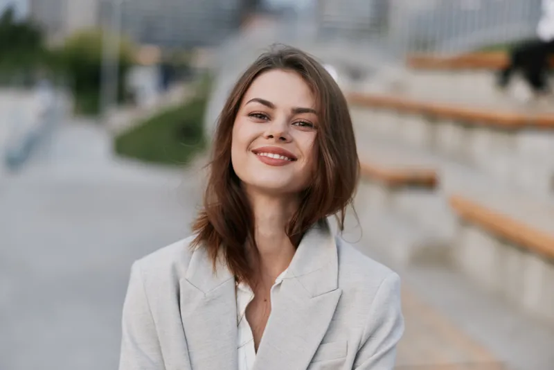Confident woman in business attire smiling outdoors, showcasing professionalism and positivity amidst a modern urban backdrop, ideal for corporate themes.