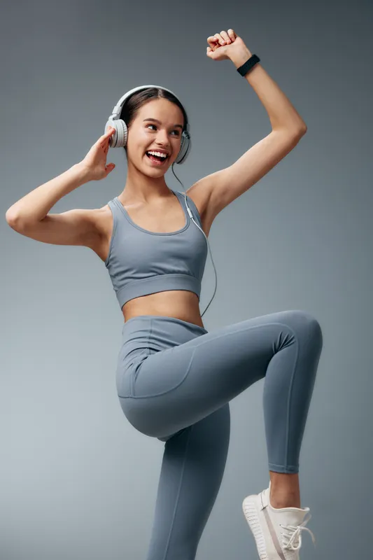 fitness, woman, sport, workout, movement in a studio shows a woman in gray athletic wear with headphones, lifting her knee and stepping, exuding energy, motivation and dynamic training.