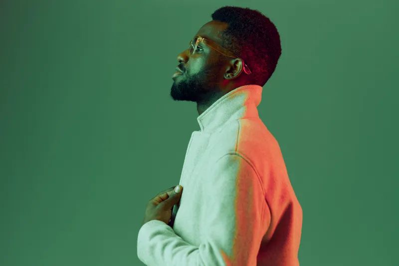 Profile portrait of a thoughtful Black man in a stylish gray sweater, showcasing a contemplative expression against a vibrant green and pink gradient background