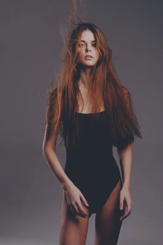 slender woman with long hair wearing black bodysuit on gray background, fashion, beauty, studio lighting