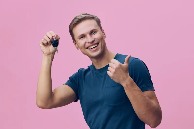 smiling young caucasian man hold key fob give thumbs up gesture wear blue t-shirt isolated pink background studio portrait digital nomad concept