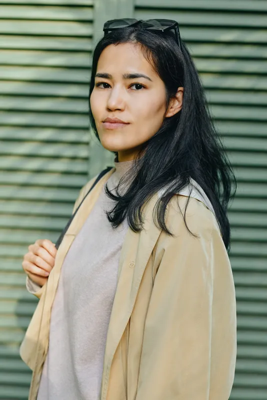 Woman in casual cardigan and light top outdoors, sunglasses resting on head, calm expression against green shutter backdrop, fashion and relaxed style for everyday wear, natural lighting and