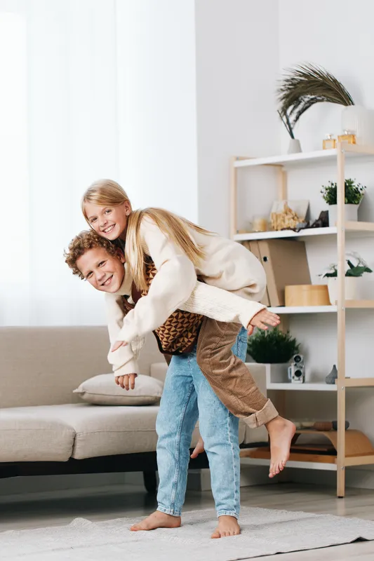 Authentic moment of play as two children share a piggyback ride at home, capturing laughter, connection, and simple joy in a cozy lifestyle setting together.