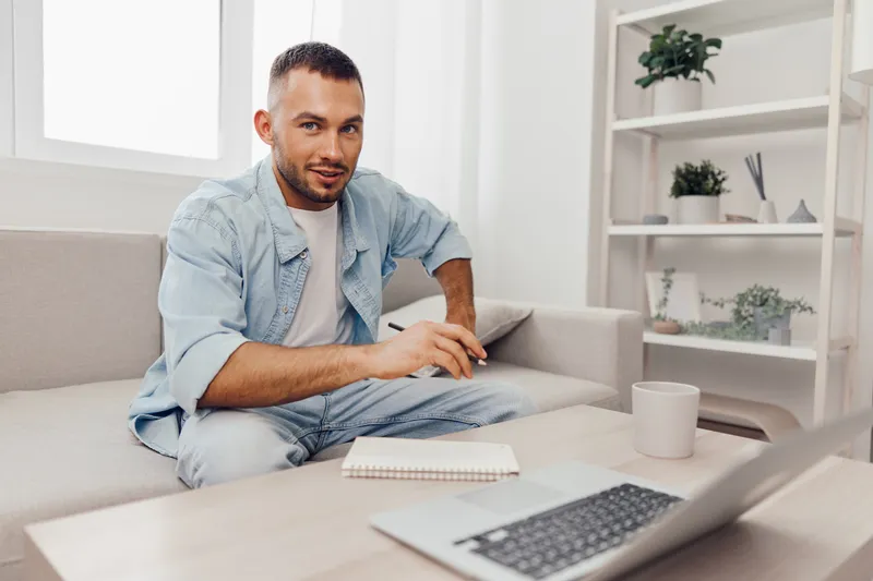 Engaging man working remotely from home, casually dressed with a notepad, exuding focus and creativity in a modern, cozy interior.