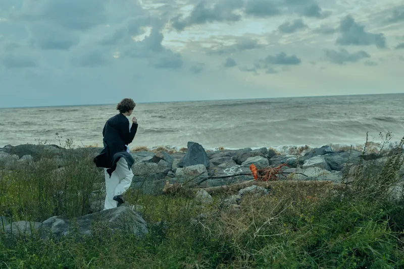 Walker on a rocky coastline gazing at the sea under an overcast sky, exploring shoreline landscape and solitude amid rugged nature