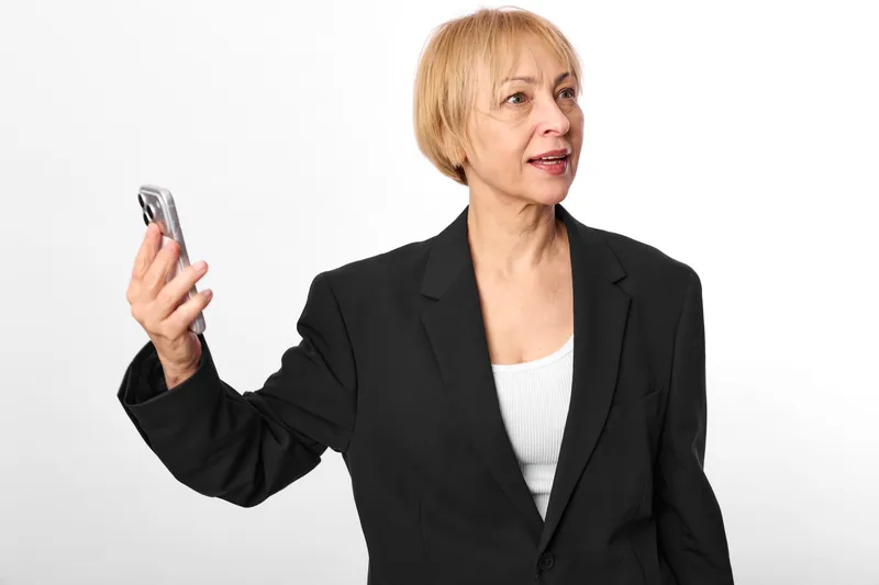 Senior businesswoman portrait holding a smartphone, looking to the side with a calm expression, communication and technology concept, isolated on white background