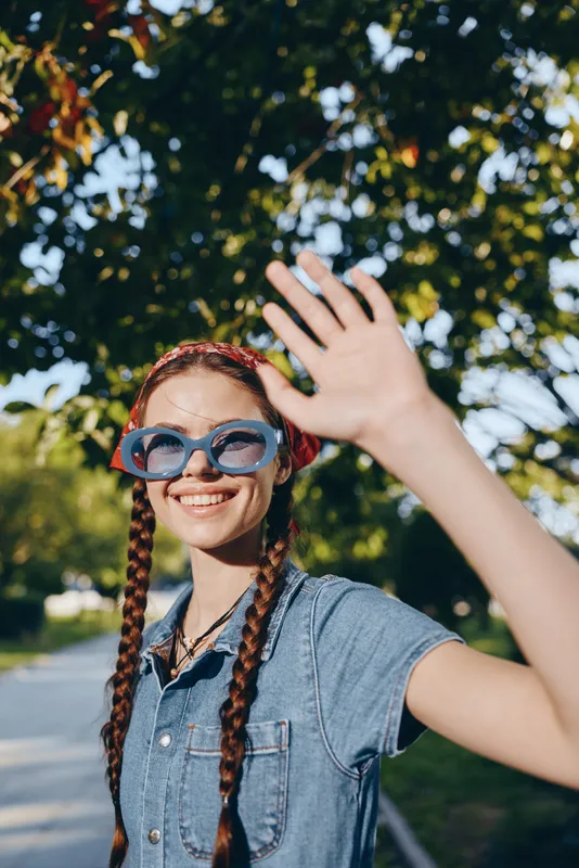 lifestyle woman in modern boho-western denim street style with braids and sunglasses, smiling outdoors in natural light with warm film color tones, casual summer vibe
