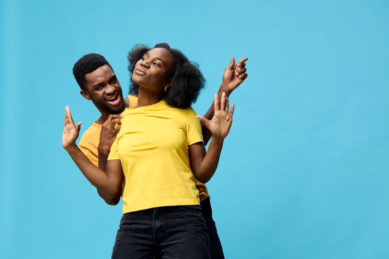 Joyful couple dancing together in matching yellow shirts against a bright blue background, expressing love and happiness, ideal for vibrant lifestyle content