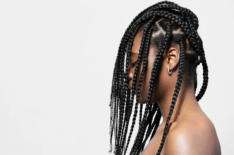 Woman with long black braided hair showcasing natural beauty and confidence against a minimalistic background, emphasizing elegance and style