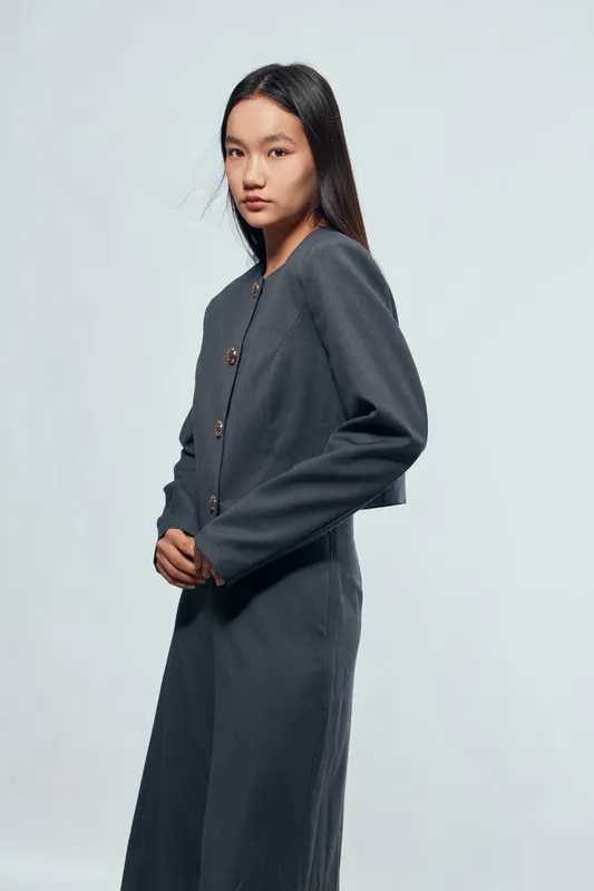 Young woman posing in dark gray comfortable cardigan and matching pants standing against light background with serious expression and natural long hair for fashion portrait.