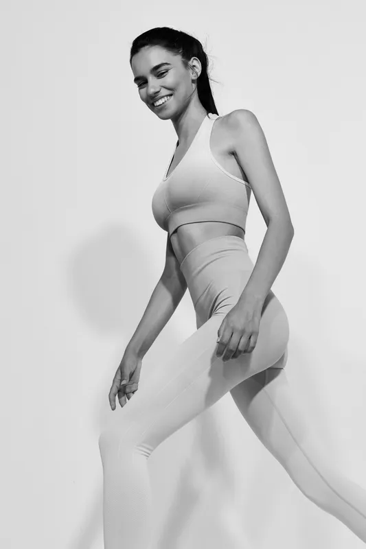 Sport fitness woman smiling in seamless activewear, showcasing healthy lifestyle and dynamic movement on a white background in black and white photography.