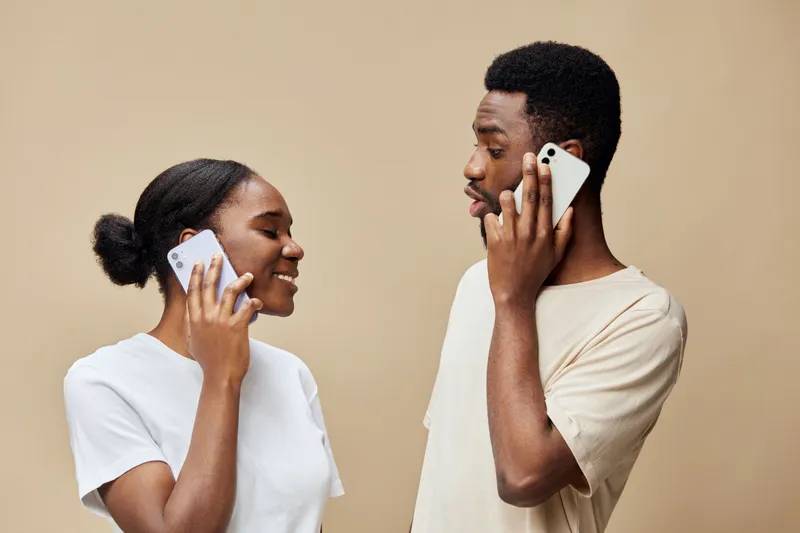 Happy diverse couple talking on smartphones against a neutral background, showcasing modern communication and connection in everyday life