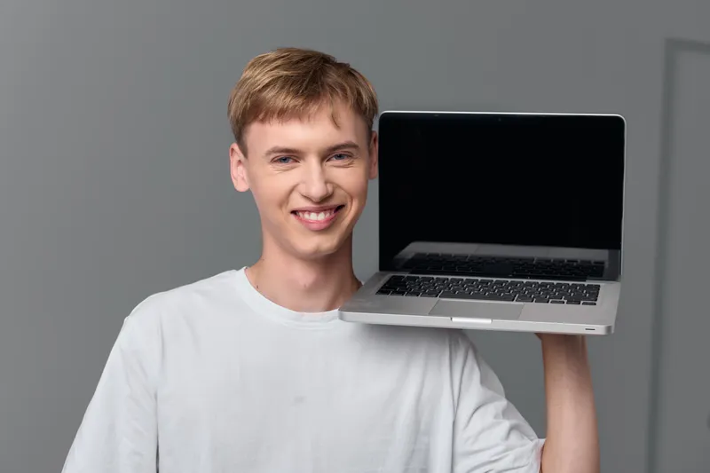 Cheerful man holding a laptop, showcasing modern technology and portable device use in a casual setting with a bright, clean background. Ideal for marketing, stock photo, advertising and social media