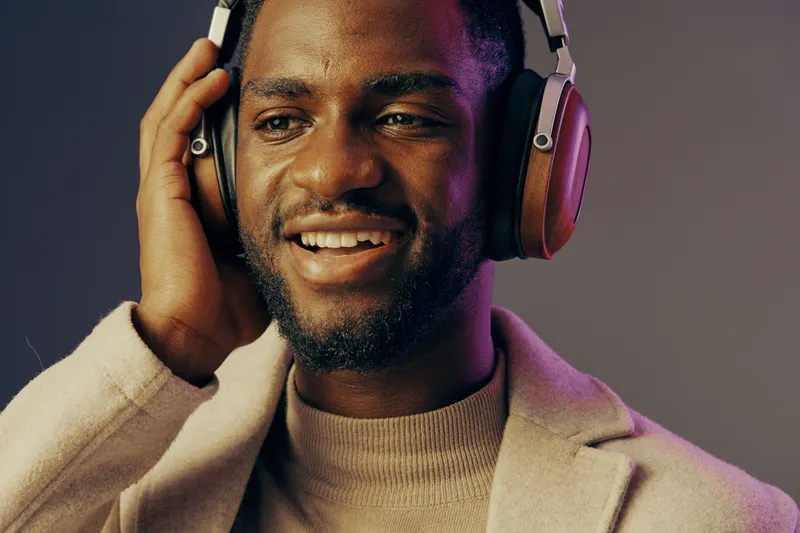 Young African man enjoying music with headphones, smiling confidently in stylish attire, showcasing a vibrant and modern urban lifestyle