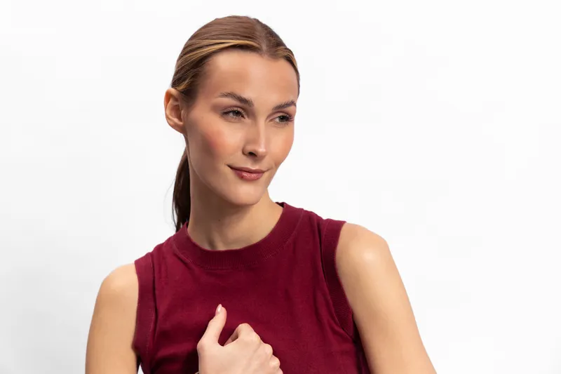Young woman with light skin and brown hair in a red sleeveless top looks to the side with a slight smile on a white background. Concept for beauty, fashion, and casual style.